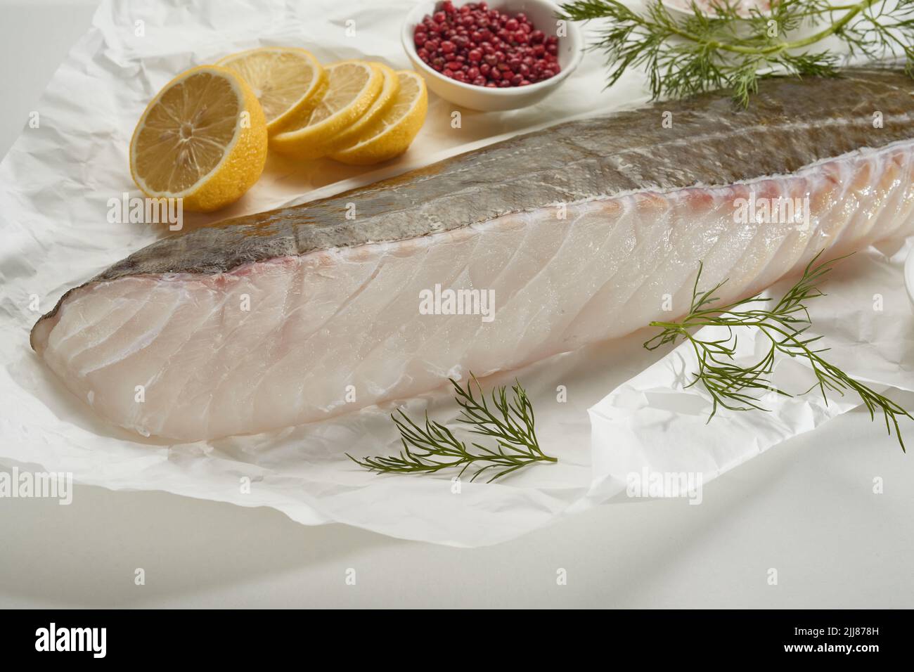 Gran ángulo de filete de pescado crudo y rodajas de limón sobre mesa blanca con pimienta y eneldo Foto de stock