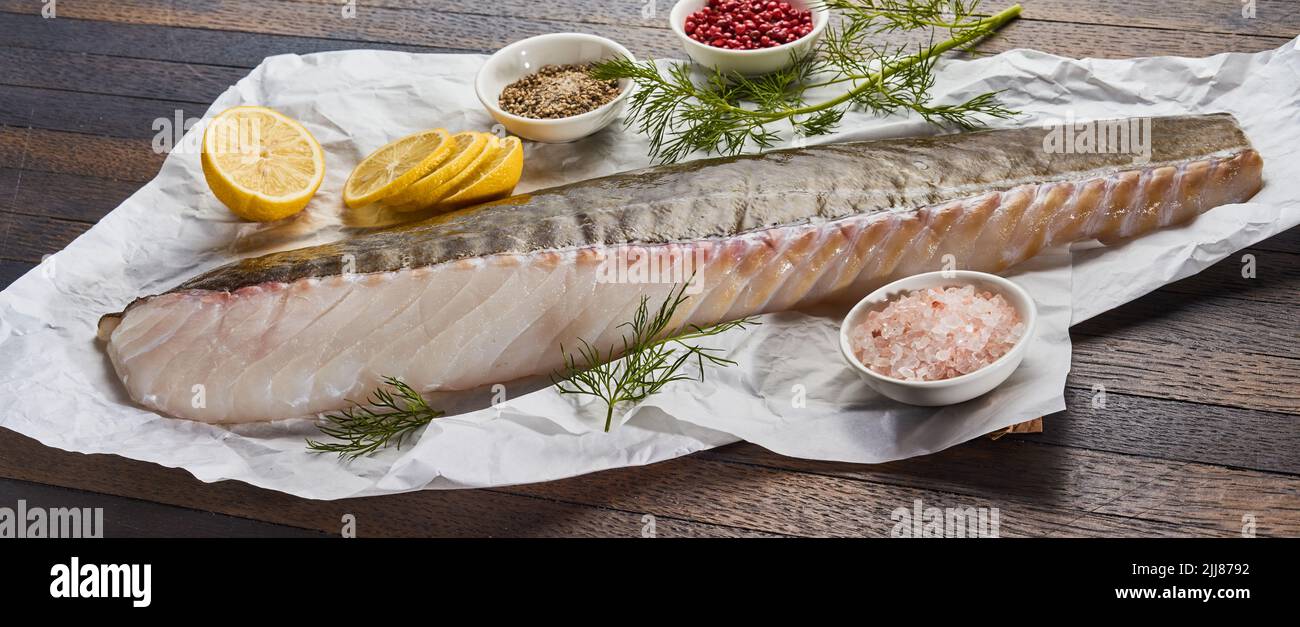 Gran ángulo de filete de pescado crudo colocado sobre la mesa con rodajas de limón y especias variadas en la cocina Foto de stock