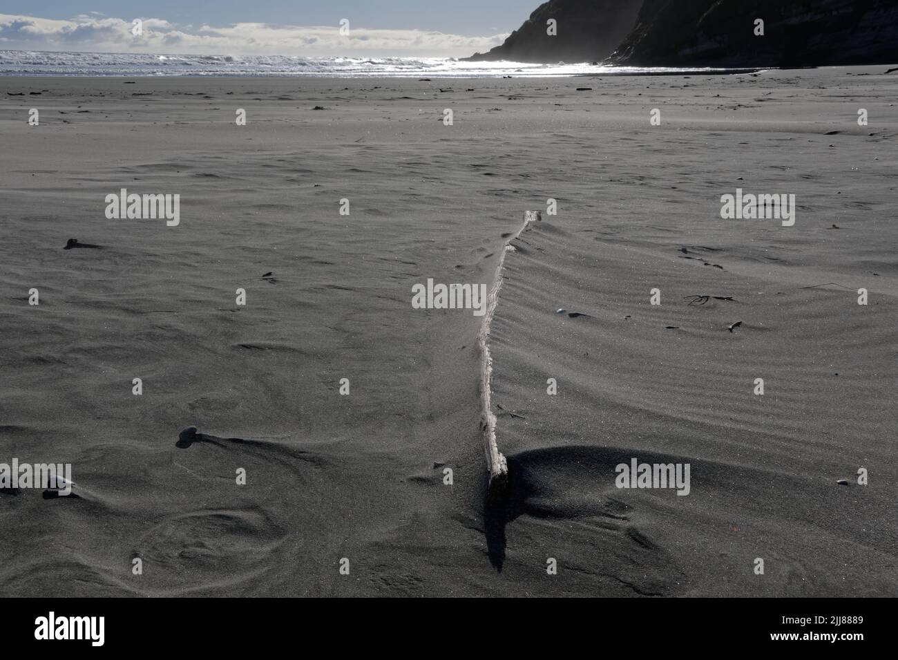 La arena se ha acumulado en un pedazo grande de madera de deriva en una playa. Los patrones del viento se muestran alrededor de las piedras en la arena. Foto de stock