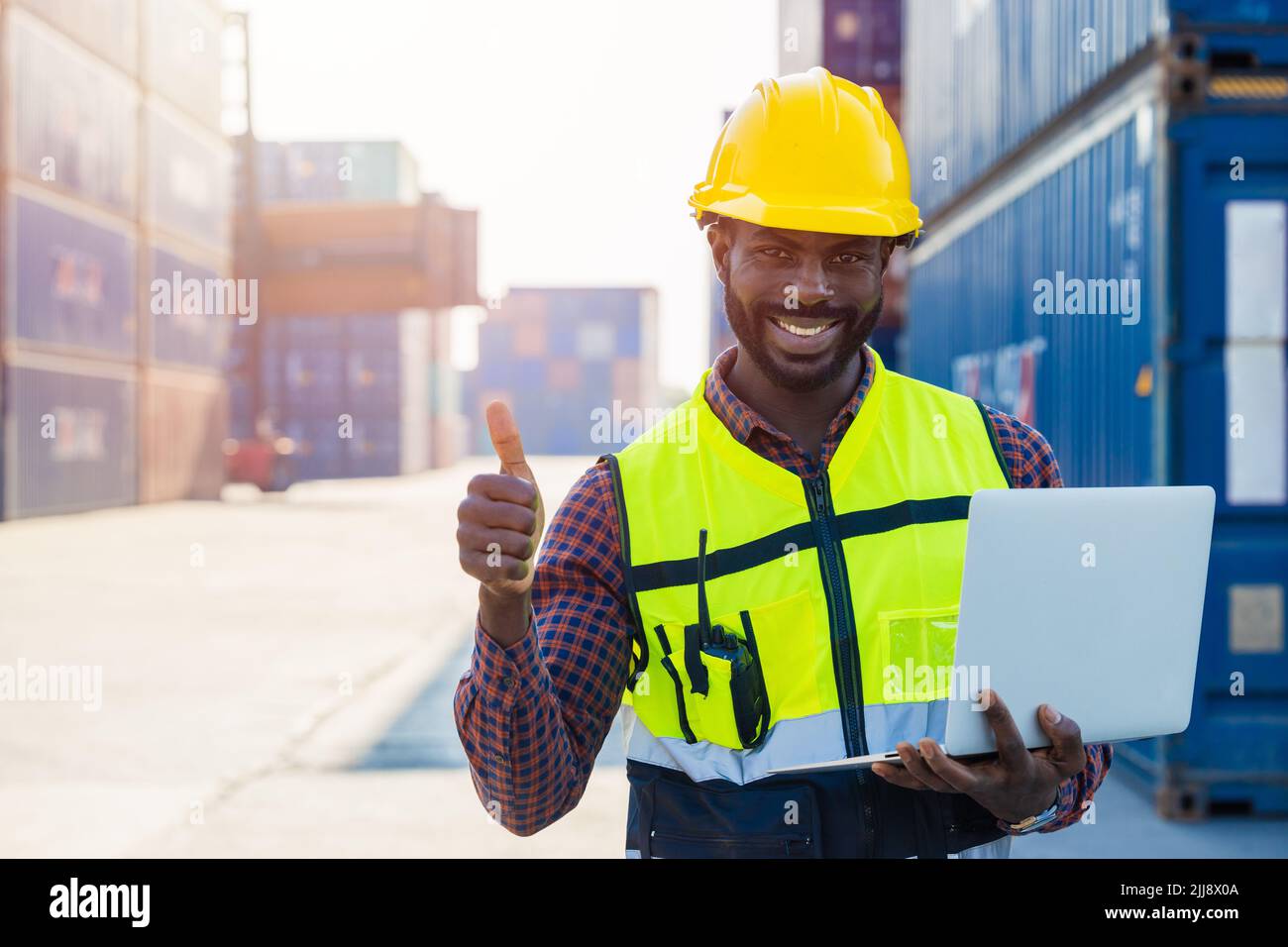 Retrato Negro africano trabajador del personal feliz sonrisa trabajando en el puerto logístico de transporte de grúa de carga con computadora portátil. Foto de stock
