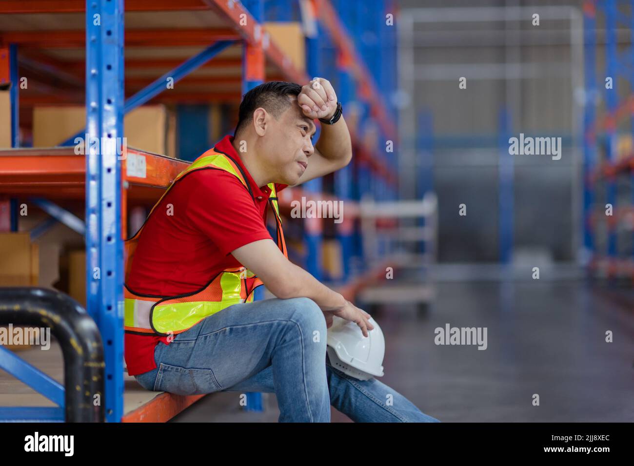 Estrés cansado Trabajador masculino asiático duro trabajo fatiga sentado descansando en la industria de inventario de carga de almacén. Foto de stock