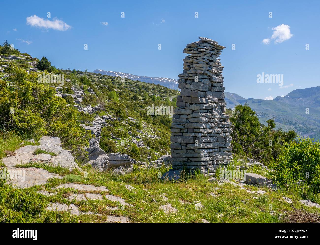 Obelisco de piedra por un sendero de montaña sobre el pueblo de Tsepelovo en la región de Zagori, al norte de Grecia, con el Monte Timfi en la distancia Foto de stock