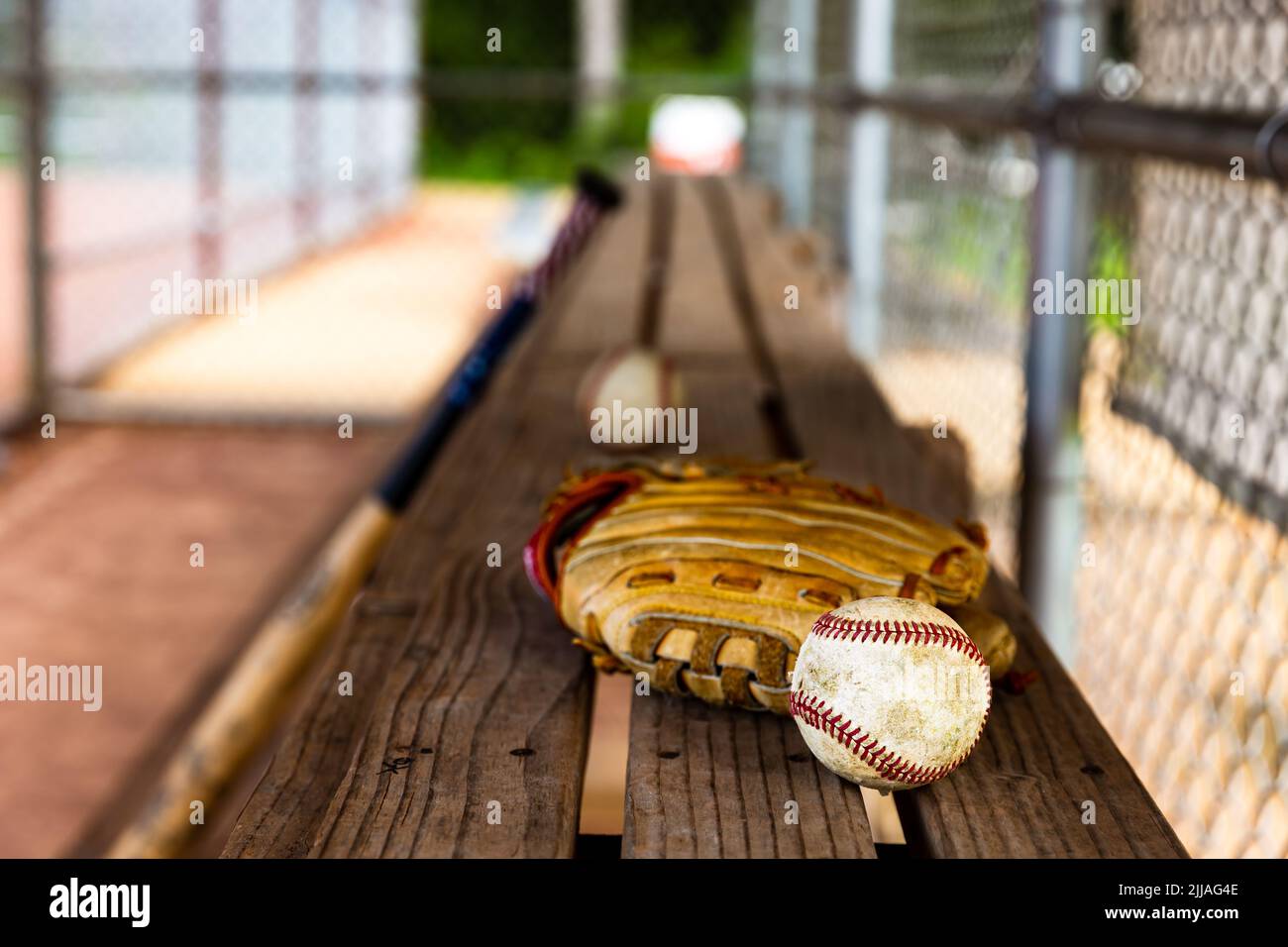 Béisbol y guante sobre banco de dugout con fondo borroso Foto de stock