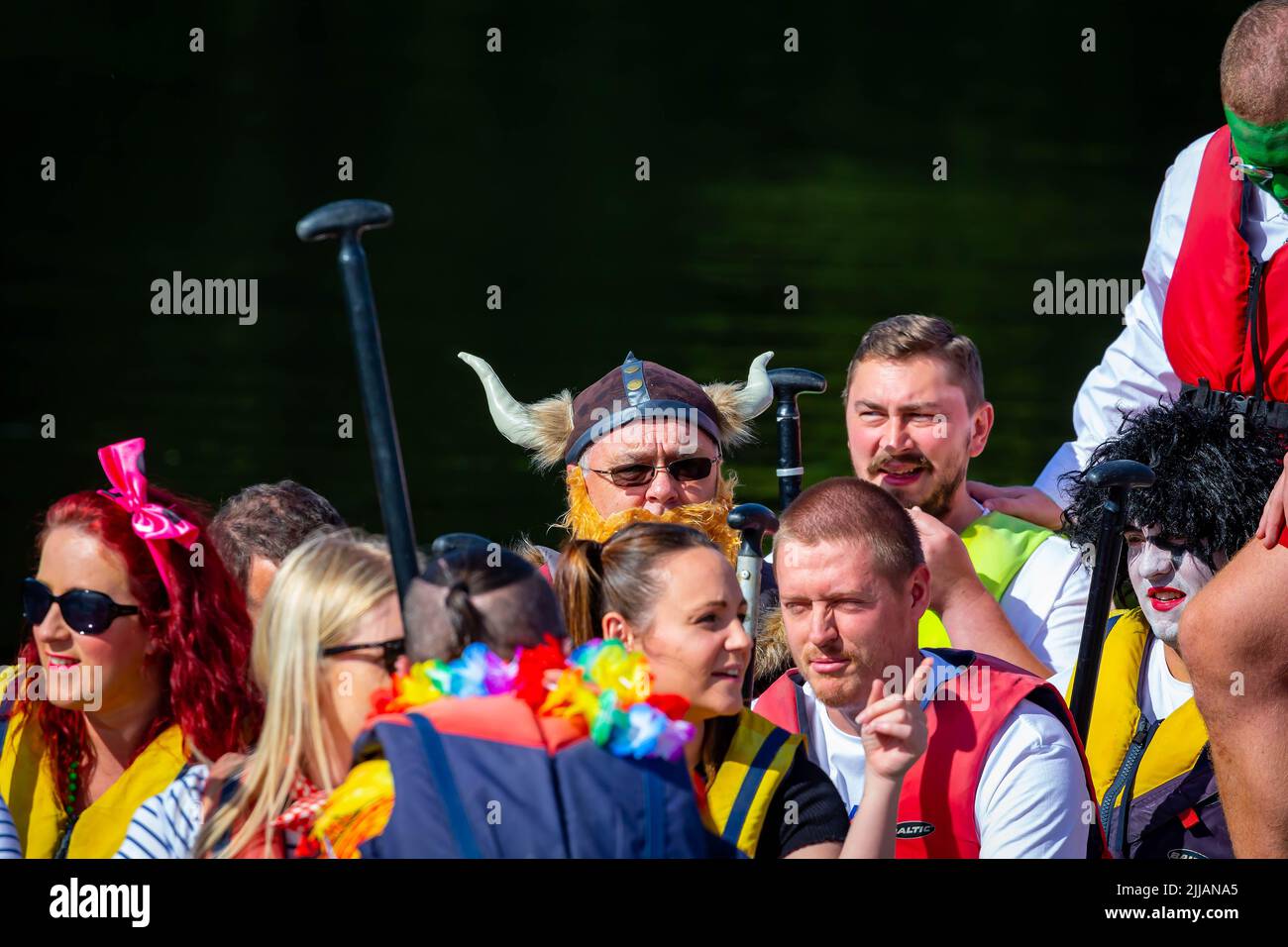 Hombre con traje vikingo con un sombrero con cuernos sentado entre colegas en una carrera de Dragon Boat Foto de stock