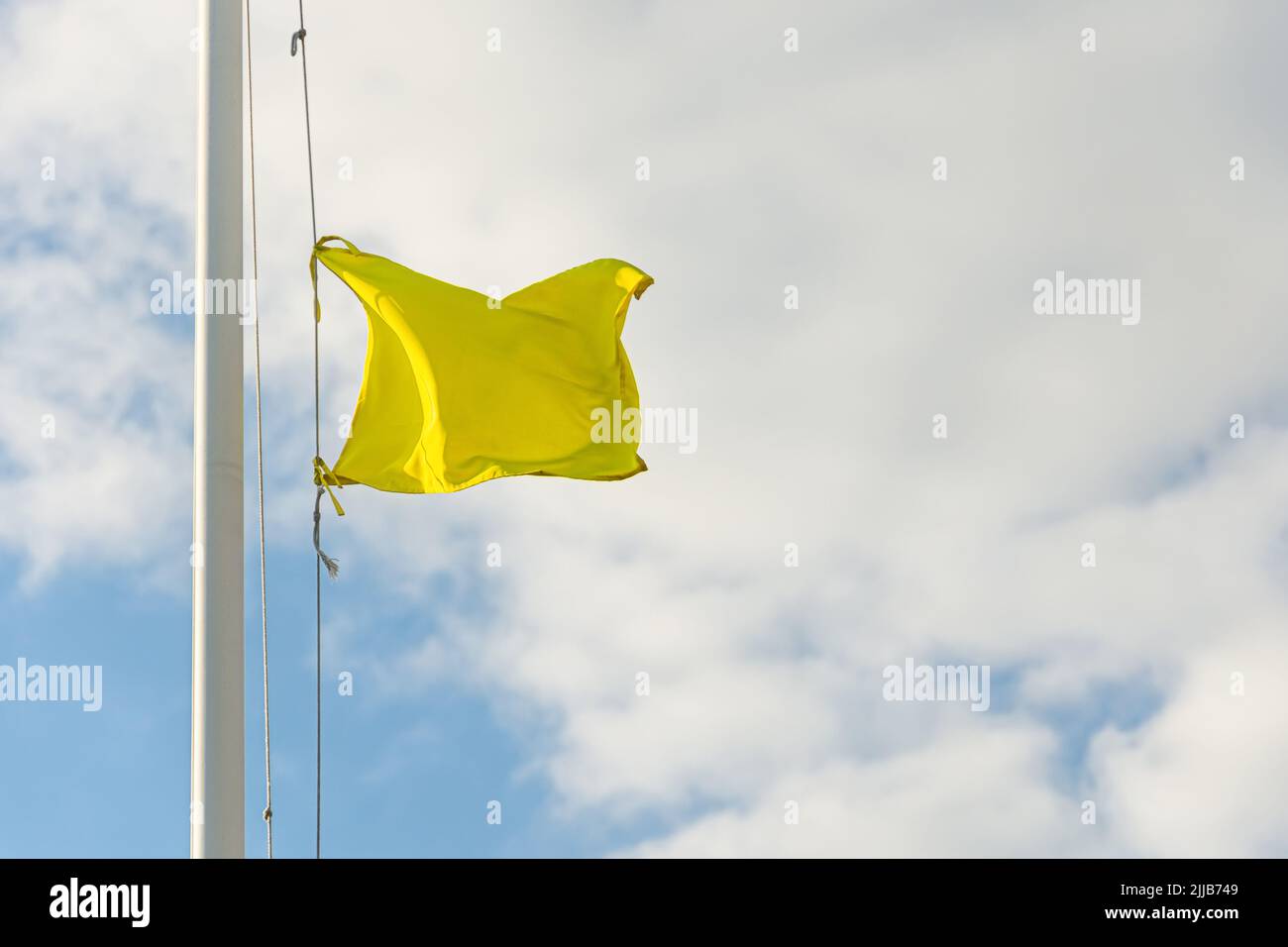 Pequeña bandera amarilla en el asta de la bandera con cielo nublado Foto de stock