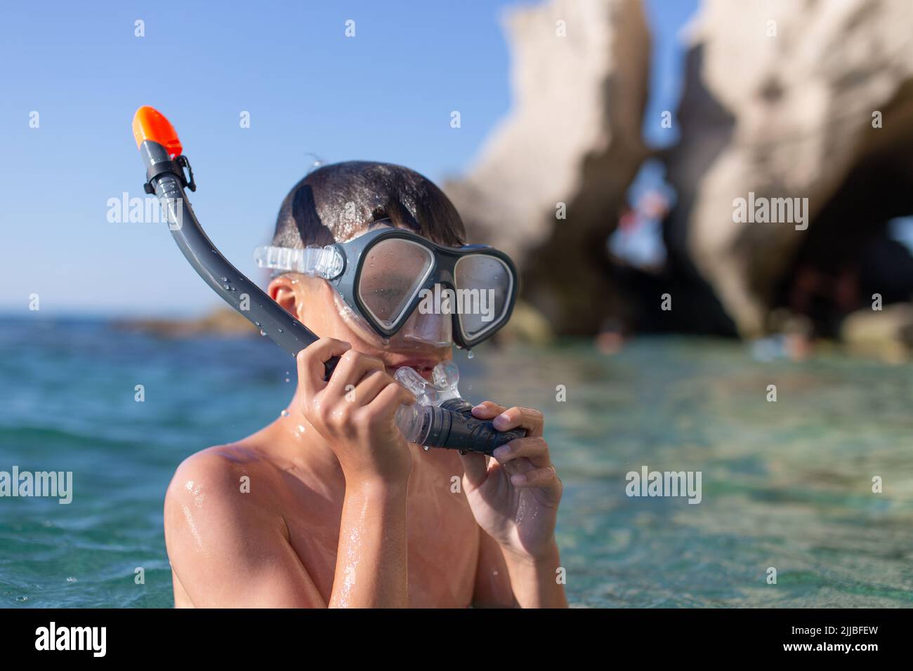 Niño en gafas de ajuste de tubo antes de bucear en la costa rocosa Foto de stock