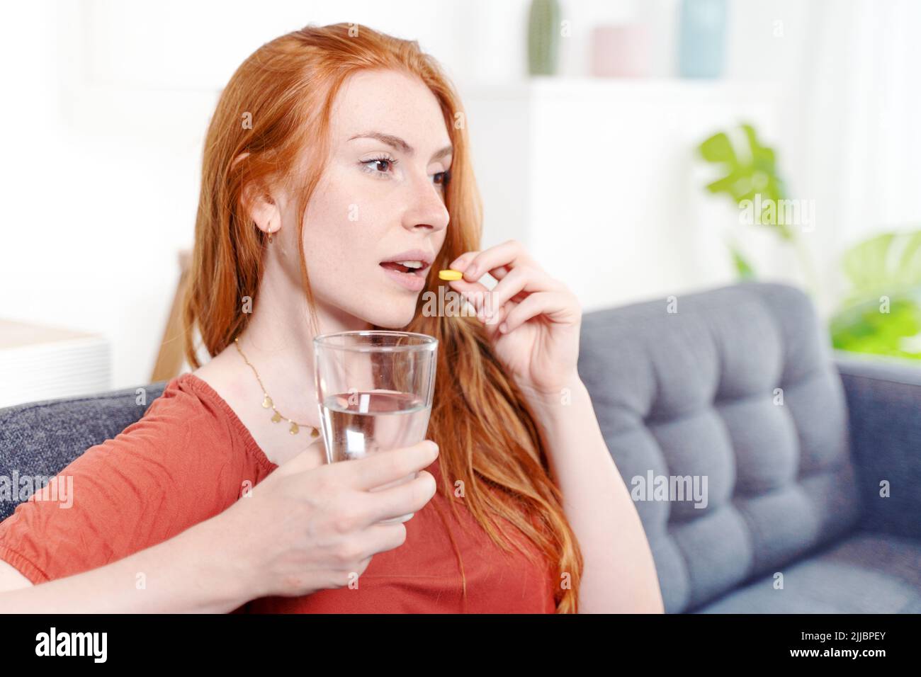 Mujer tomando vitaminas mientras se sienta en el sofá en casa Foto de stock