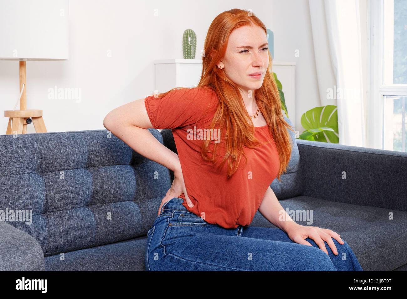 Mujer sentada en un sofá y sufre de dolor de espalda baja Foto de stock