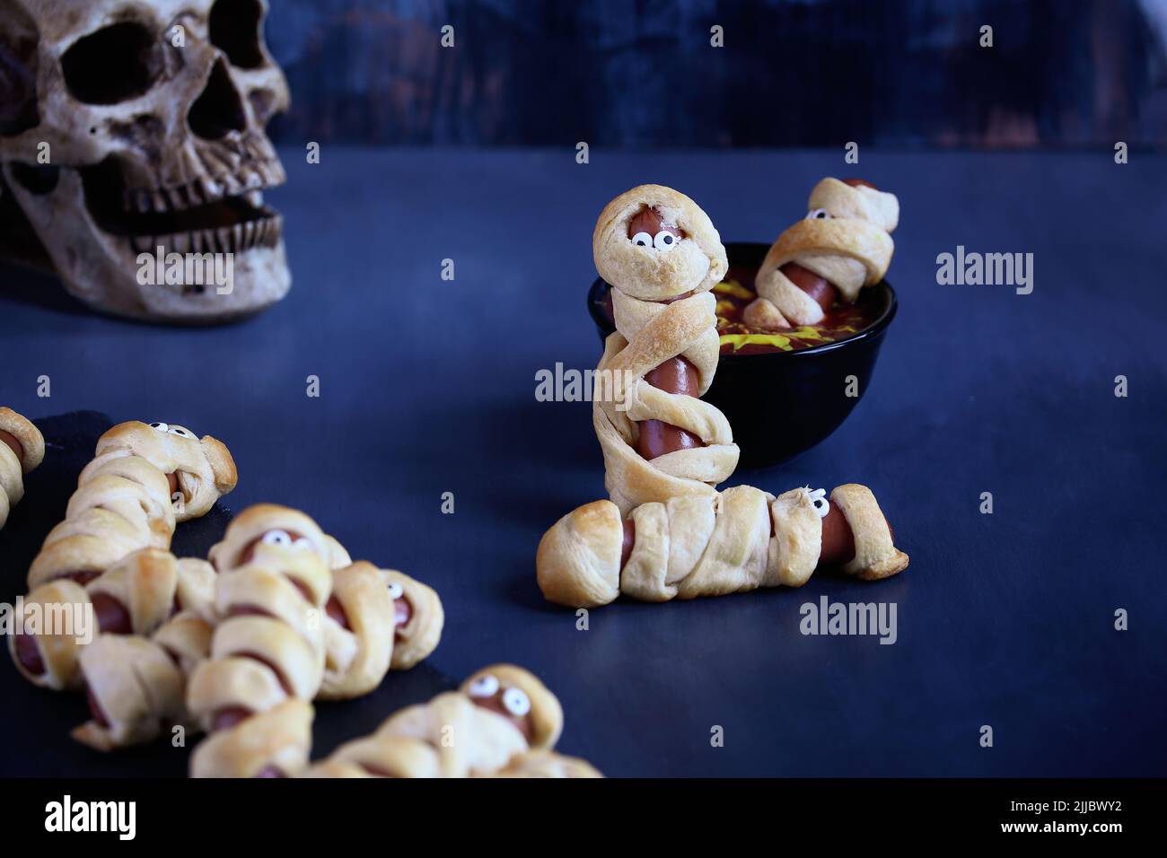 Comida divertida para los niños. Momia los perros calientes (o los cerdos en una manta) en una mesa rústica azul con un tazón de ketchup y salsa de mostaza, con diseño de tela de araña. Blurre Foto de stock
