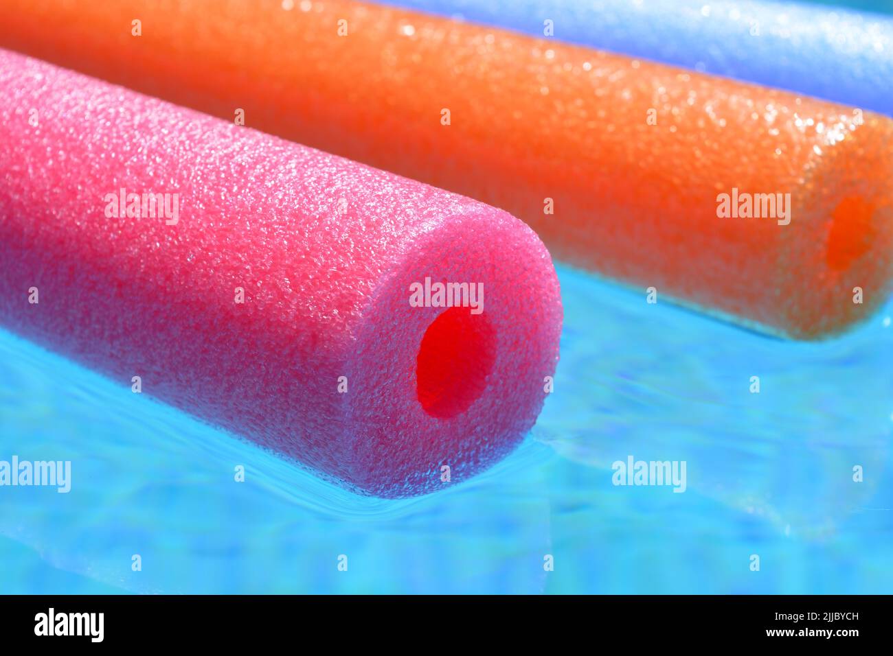 Vibes de verano, fideos coloridos de polietileno rosa, naranja y azul flotando en la piscina Foto de stock
