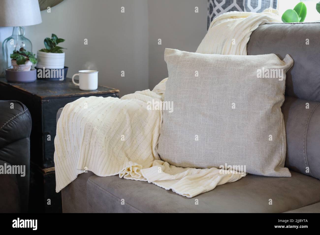 Suave manta de punto blanco lanza sobre el brazo de un sofá gris en un salón de estilo de granja. Enfoque selectivo con fondo borroso. Foto de stock