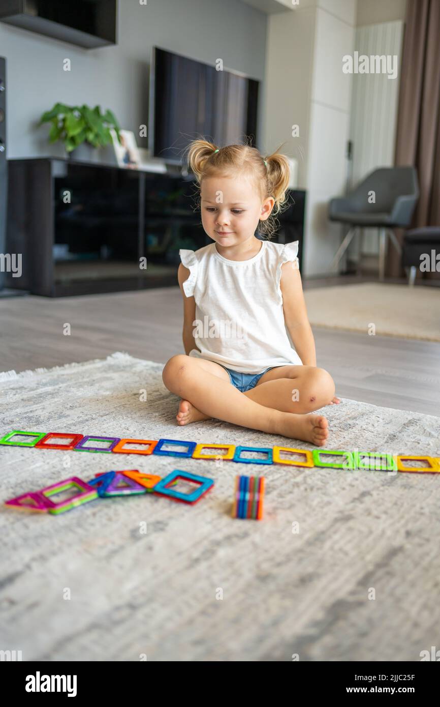 Pequeña niña jugando a bloques de plástico imán colorido kit en casa. El niño juega juegos educativos. Desarrollo de la primera infancia. Foto de stock