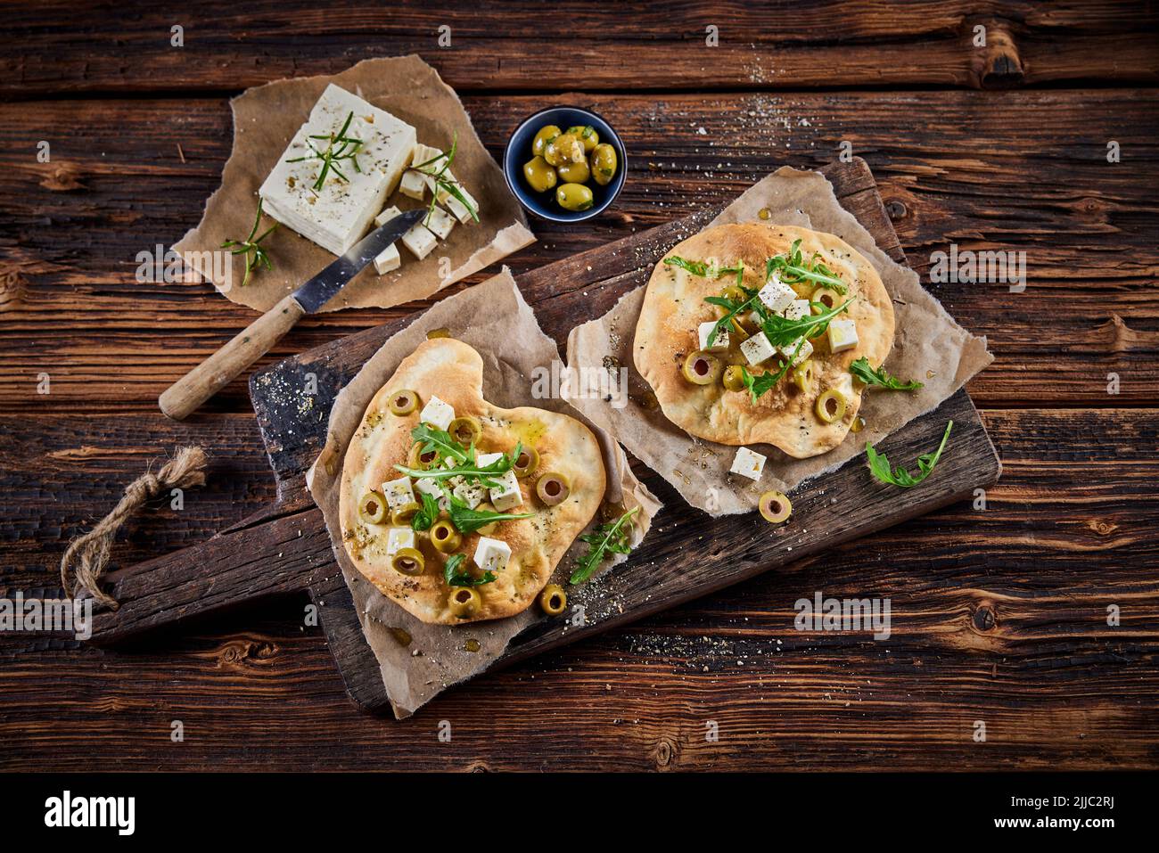 Vista superior de un delicioso plato con pan de pita crujiente adornado con aceitunas de queso feta y hierbas servidas sobre una tabla de madera en la mesa Foto de stock
