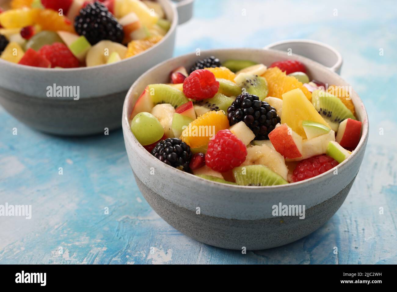 Frutas picadas frescas y sabrosas y bayas maduras de colores servidas en cuencos de cerámica sobre una mesa de madera en una cocina ligera en casa Foto de stock