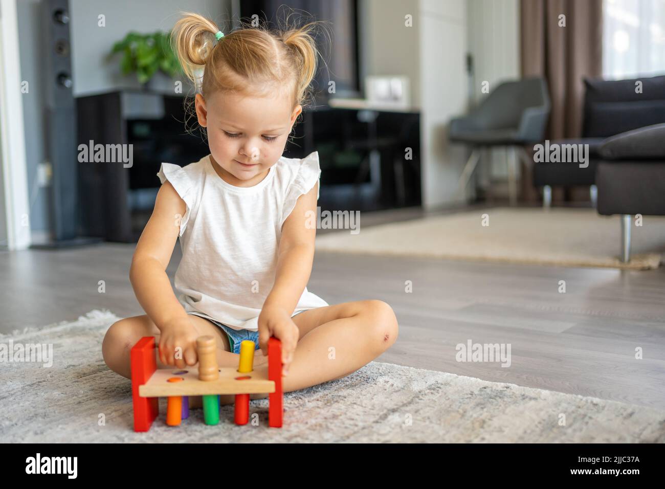 Bonita niña caucásica jugando en el suelo en casa con juguetes de madera ecológicos. Juguete Montessori. El niño jugando juegos educativos. Foto de stock