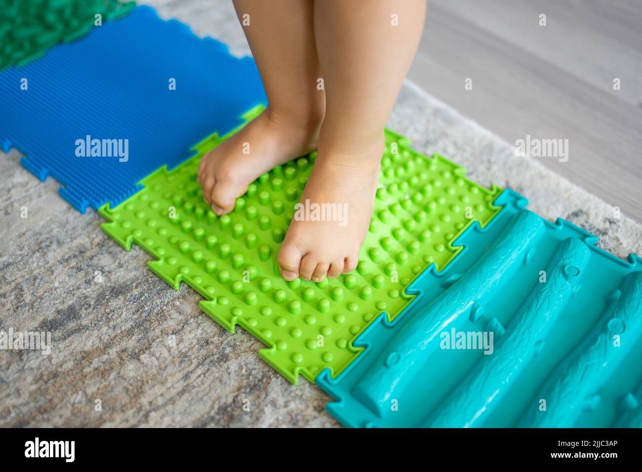 Vista de cerca de los paseos de niña en una alfombra de masaje. Alfombrilla de masaje de pies para bebés. Ejercicios para piernas alfombra de masaje ortopédico. Foto de stock