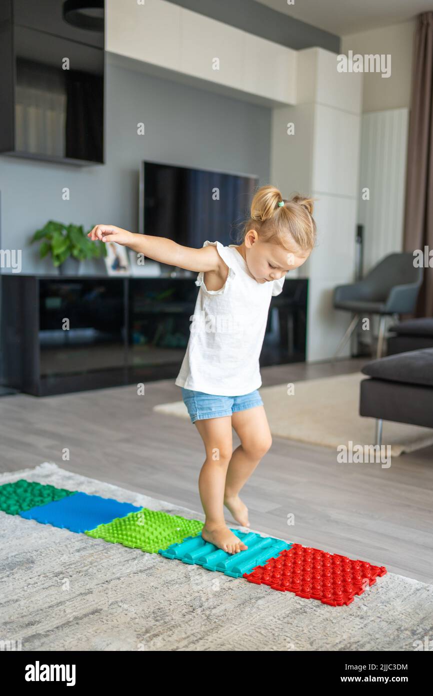 Una niña pequeña camina sobre una alfombra de masaje. Alfombrilla de masaje de pies para bebés. Ejercicios para piernas alfombra de masaje ortopédico. Foto de stock
