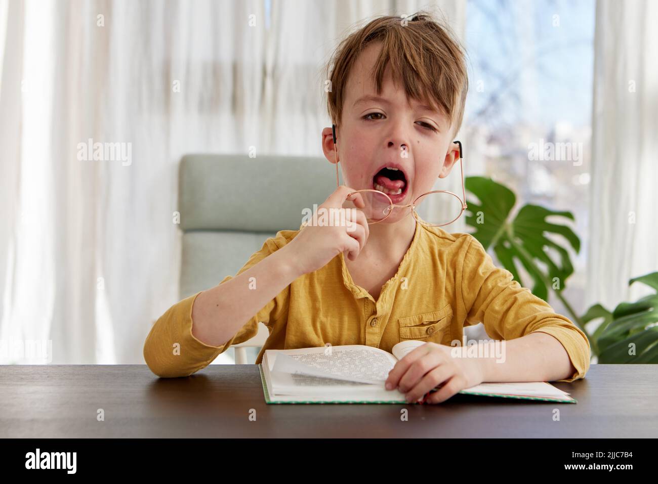 Un pequeño estudiante aburrido bostezando durante la lectura en casa Foto de stock