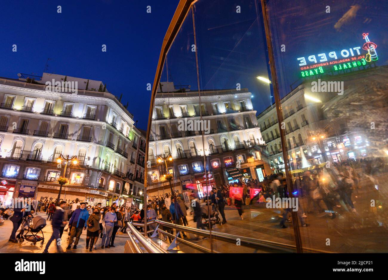 Multitudes en la Puerta del Sol, por la noche con el famoso cartel publicitario Tio Pepe reflejado en las ventanas de la estación de metro Sol. Madrid, España. Foto de stock