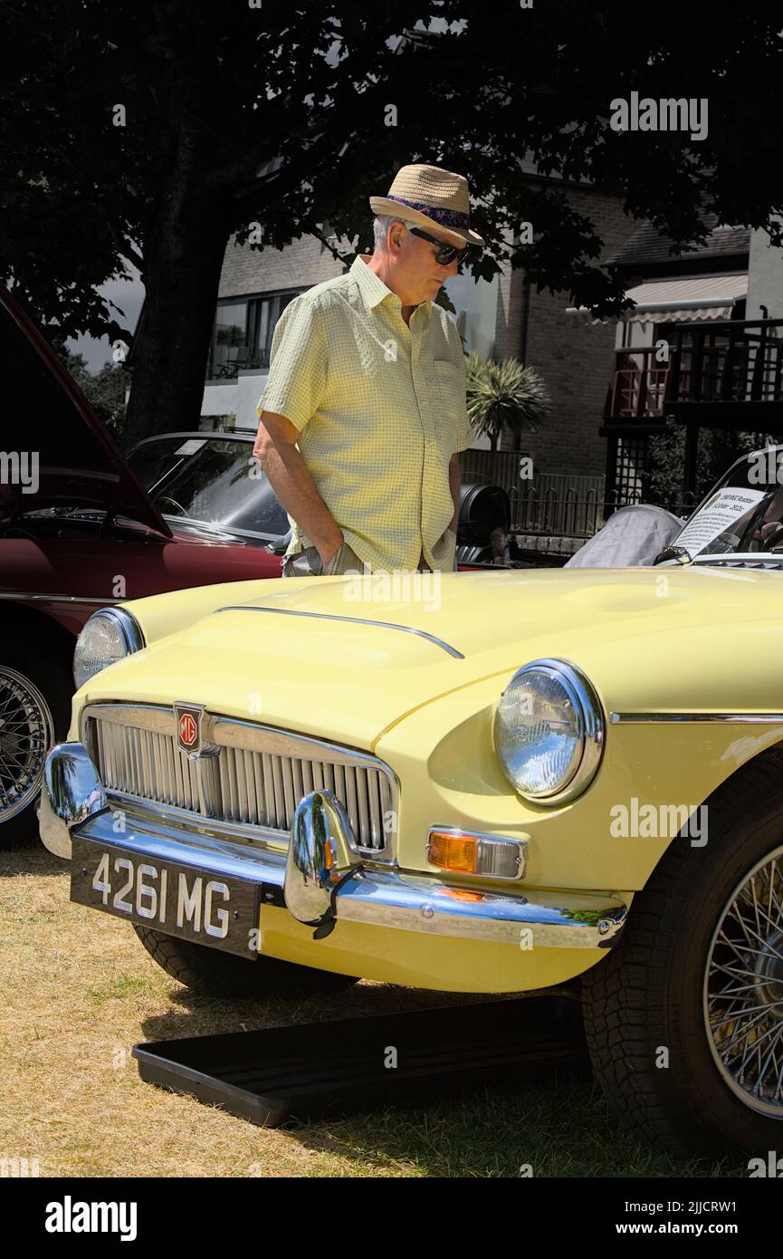 Hombre con sombrero de paja en colores que combinan admirando Un coche deportivo clásico MGC 1968 amarillo Roadster, Christchurch, Reino Unido Foto de stock