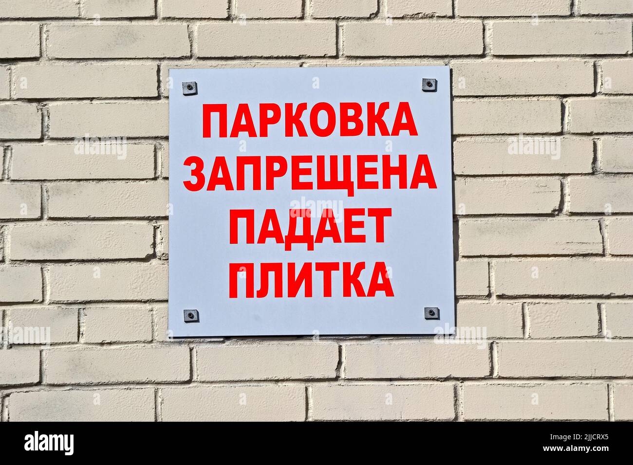 aparcamiento prohibido. caída de azulejos como mensaje de texto rojo en ruso en la pared de ladrillo, advertencia de seguridad diversidad Foto de stock