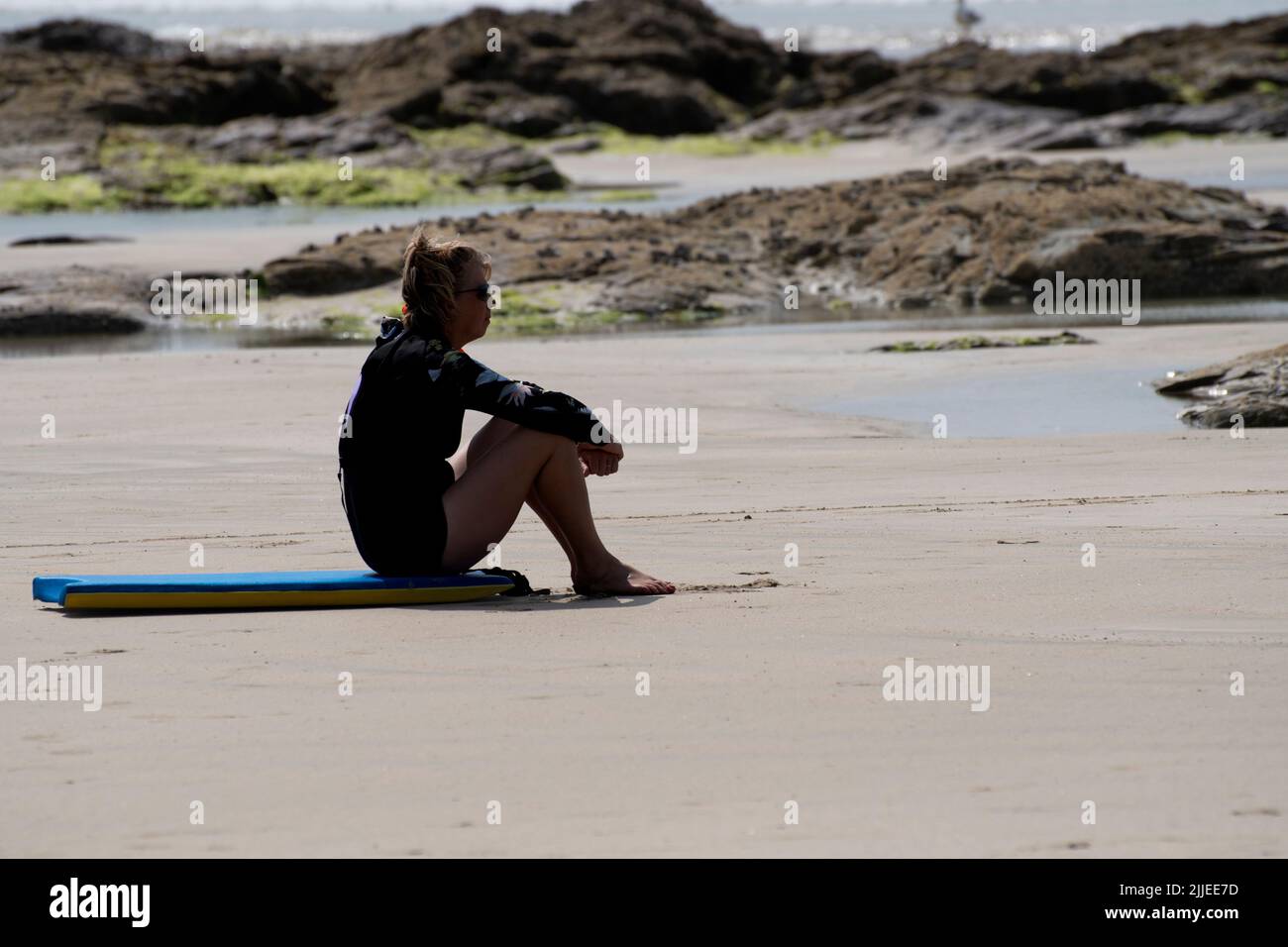 Polzeath, Reino Unido - Julio de 18 2022 - Una joven surfista se sienta en su tablero del cuerpo esperando las olas correctas en la playa de Polzeath Foto de stock