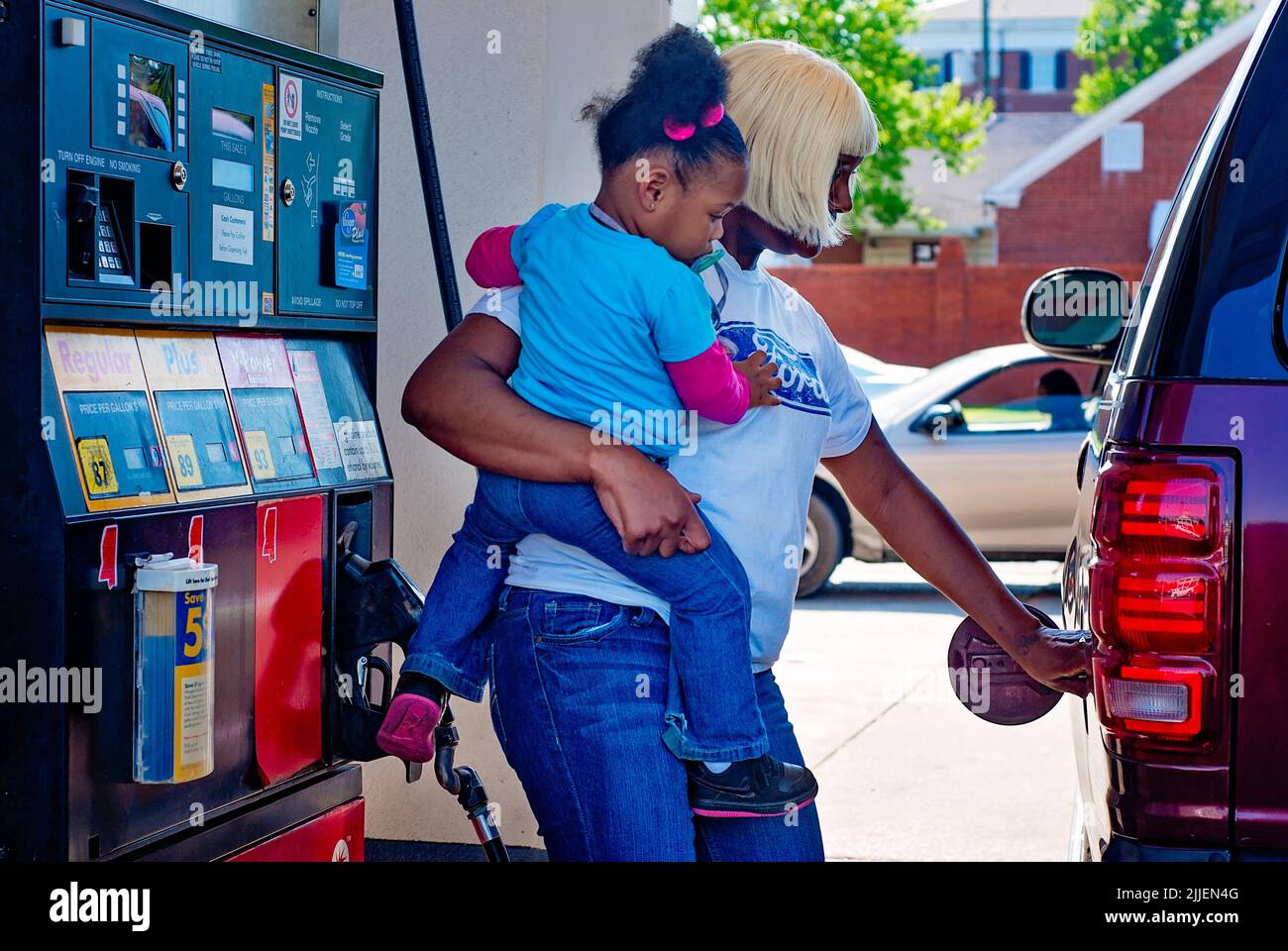 Una mujer bombea gas mientras sostiene a su hija, el 14 de abril de 2011, en Columbus, Mississippi. Los precios del gas aumentaron en 2011 debido al debilitamiento del dólar estadounidense. Foto de stock