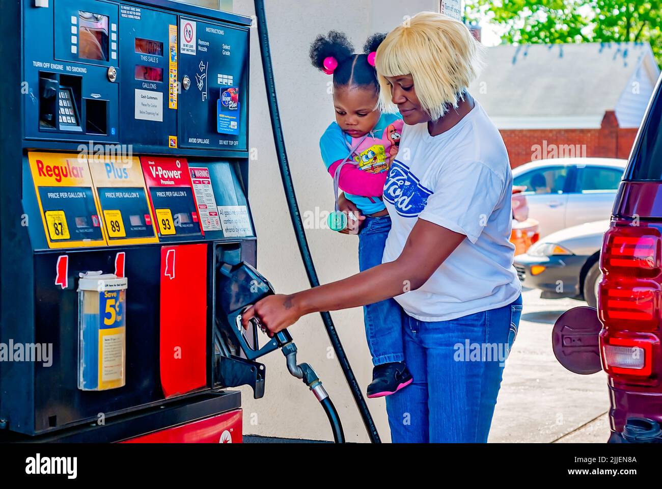 Una mujer bombea gas mientras sostiene a su hija, el 14 de abril de 2011, en Columbus, Mississippi. Los precios del gas aumentaron en 2011 debido al debilitamiento del dólar estadounidense. Foto de stock