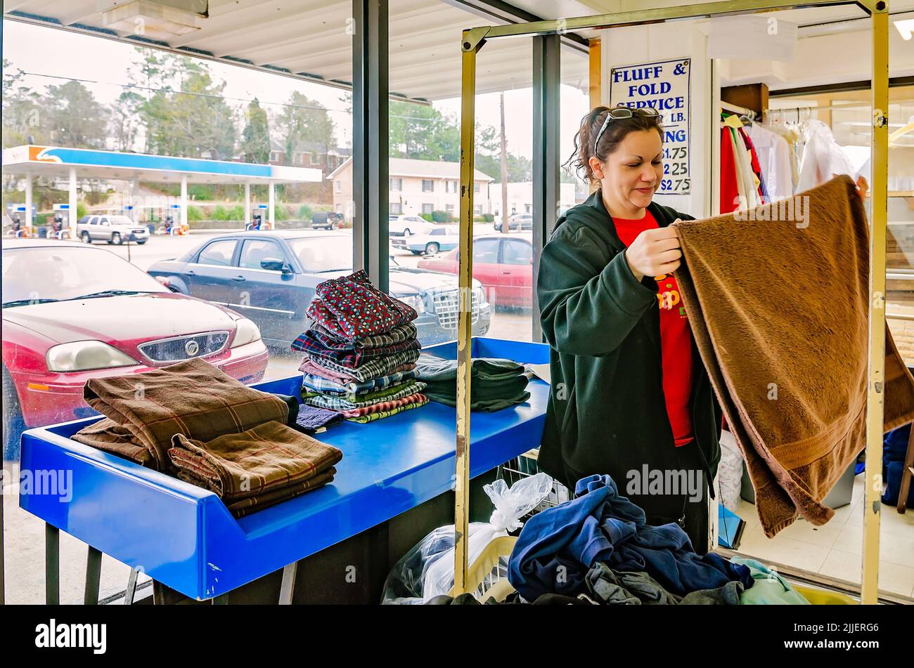 Una mujer dobla la ropa en una lavandería automática, el 23 de febrero de 2013, en Columbus, Mississippi. El trabajo paga el salario mínimo. Foto de stock