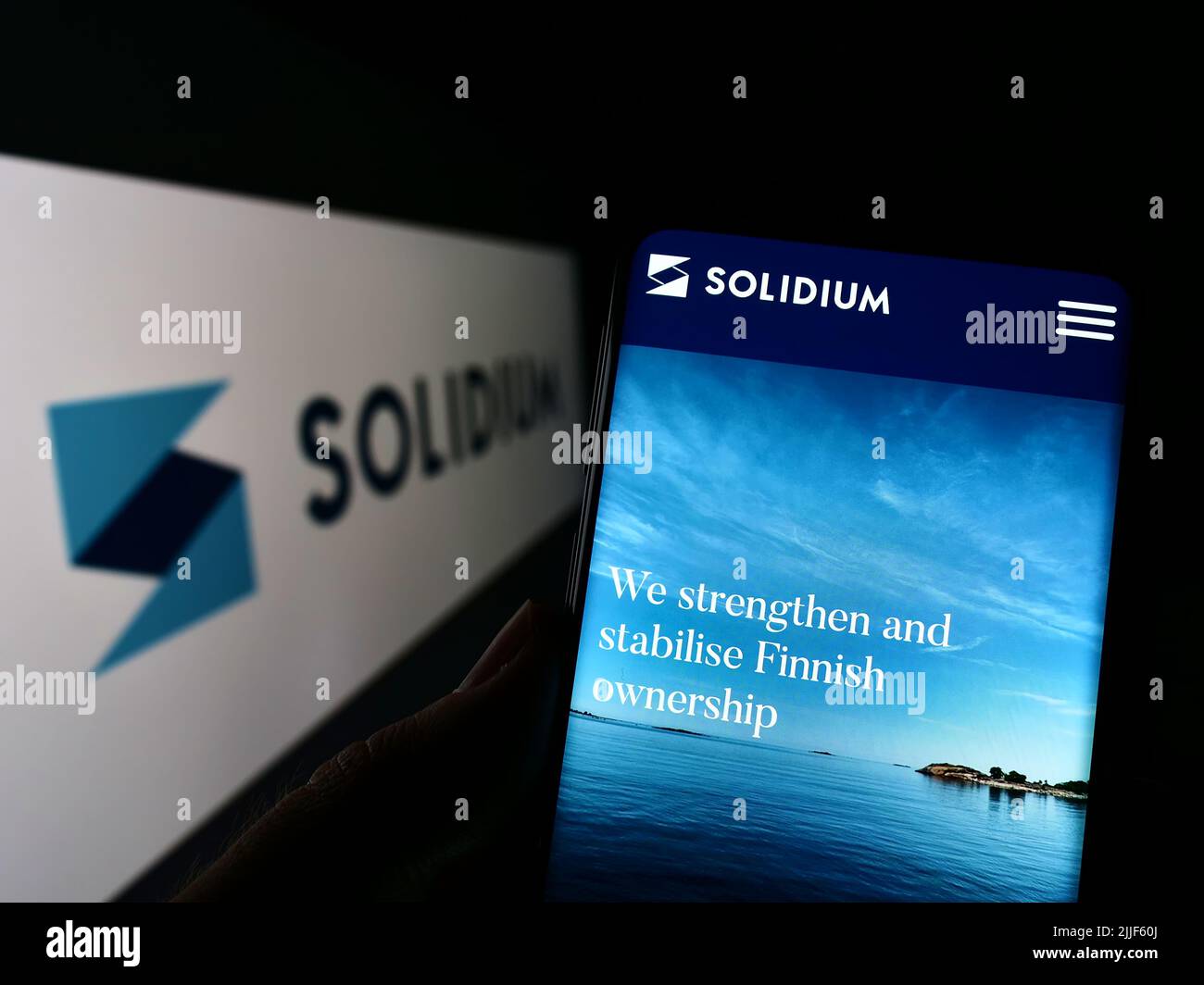Persona que sostiene el teléfono móvil con la página web de la empresa de inversión finlandesa Solidium Oy en la pantalla delante del logotipo. Enfoque en el centro de la pantalla del teléfono. Foto de stock