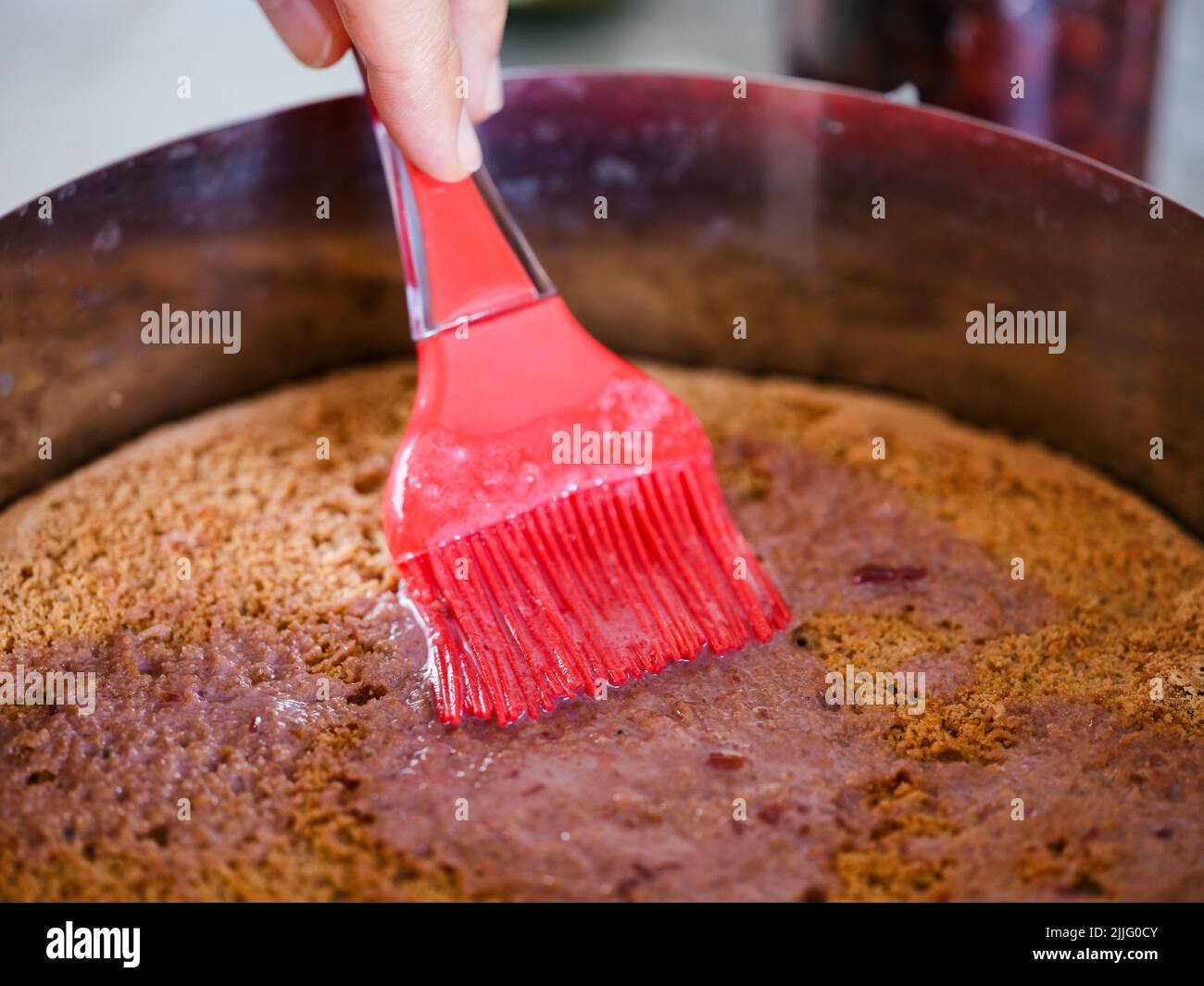 Una mujer aplicando jarabe en medio de un bizcocho casero sin gluten con un cepillo de cocina Foto de stock