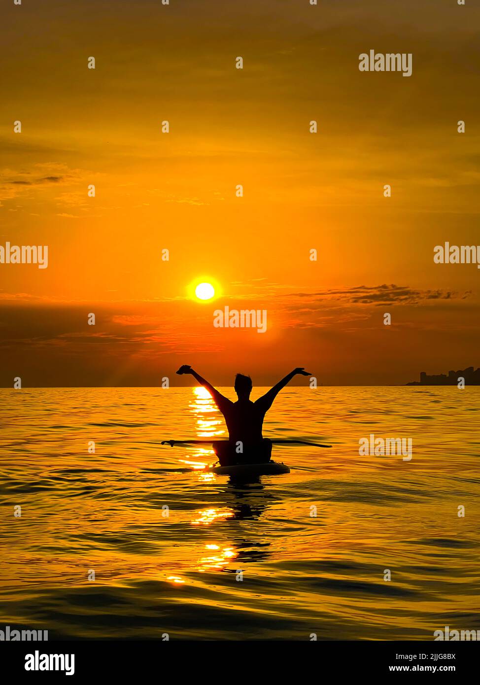 silueta de una alegre niña feliz manos para arriba en el mar en la puesta de sol a bordo sup. Foto de stock