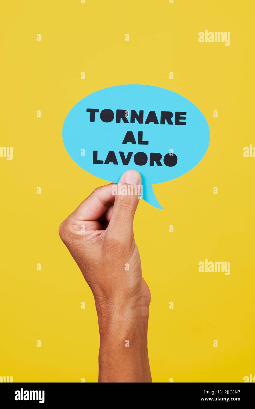 el hombre sostiene una señal de papel azul en forma de burbuja de discurso con el texto escrito de nuevo al trabajo en italiano, sobre un fondo amarillo Foto de stock