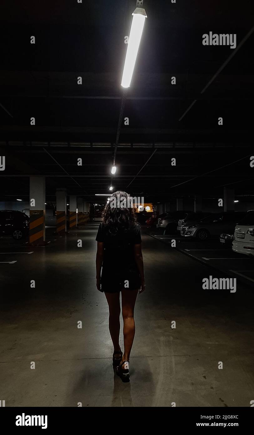 una chica camina por el aparcamiento por la noche. foto vertical. Foto de stock
