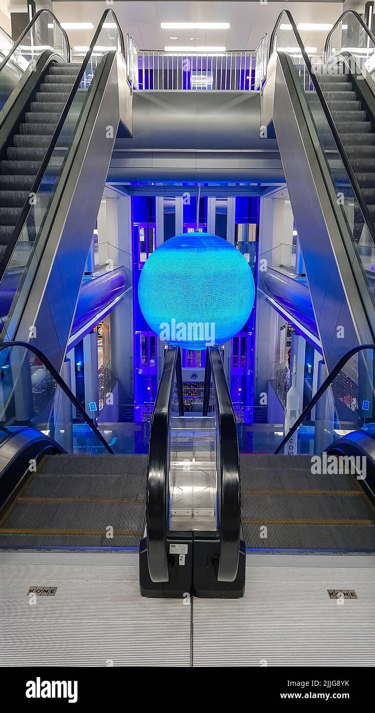 Una moderna escalera mecánica en un edificio de tiendas y entretenimiento. El holograma del planeta está en el centro de atención. Foto vertical Foto de stock
