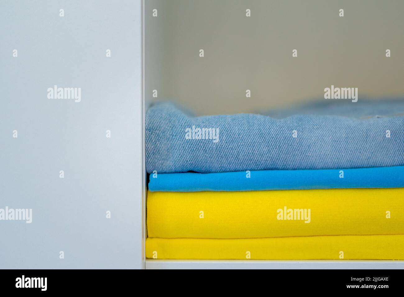 La ropa de colores brillantes se apilan cuidadosamente. Los colores amarillo y azul de la bandera ucraniana en el armario. Foto de stock