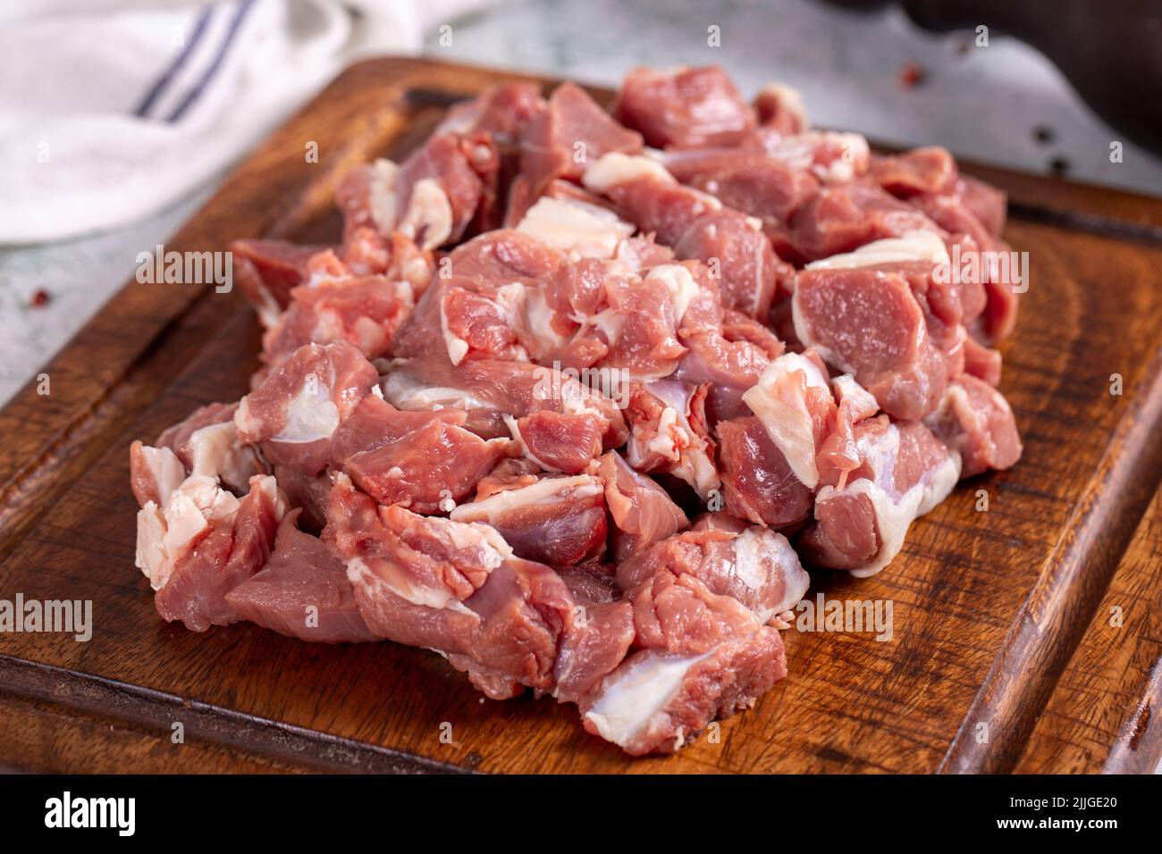 Carne de cordero en cubitos. Carne roja cortada en un plato de madera sobre un fondo de piedra. Productos de carnicero. Primer plano Foto de stock