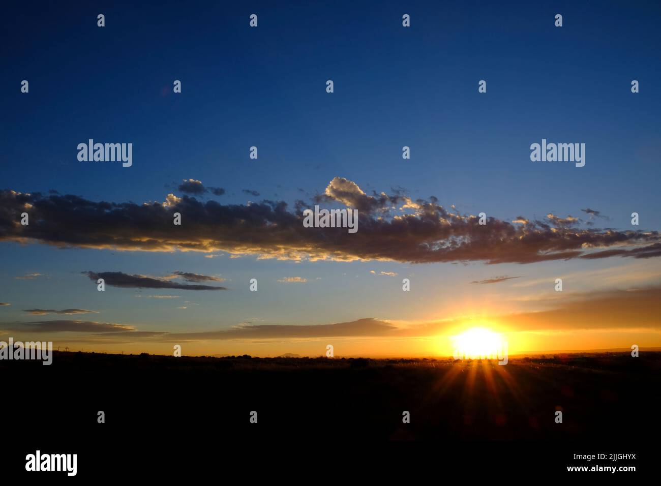 La puesta de sol o la salida del sol se levanta con la estrella del sol y los rayos de luz dorada y las nubes en el cielo azul Foto de stock