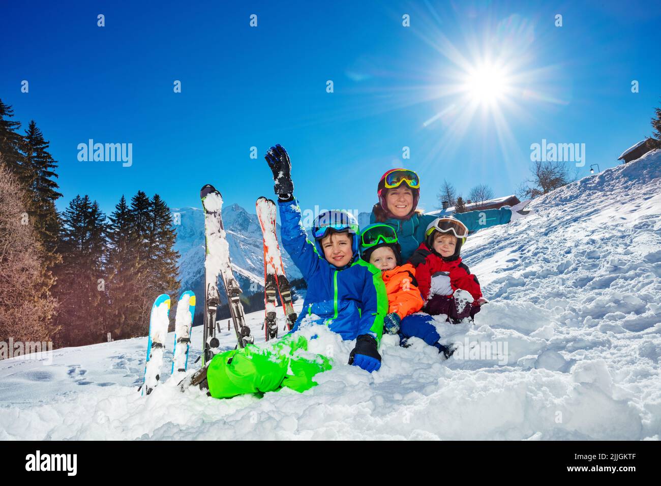 Los niños y la madre - La familia de vacaciones de esquí se sientan juntos en la nieve Foto de stock