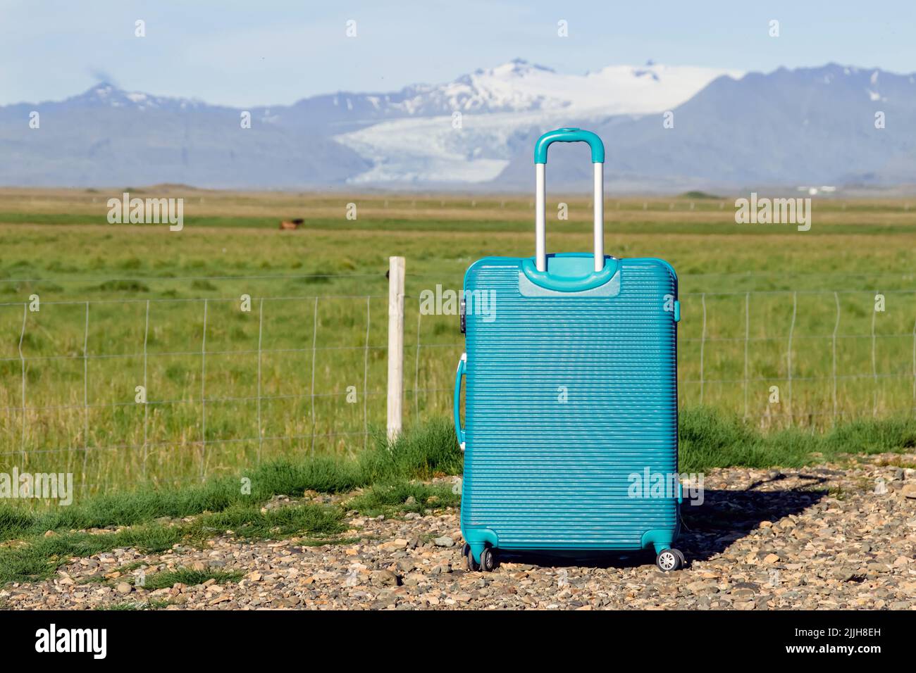 Maleta de equipaje azul individual frente a pastos verdes y montañas con glaciar en días soleados y cielo azul. Mucho espacio de copia en la cara. Foto de stock