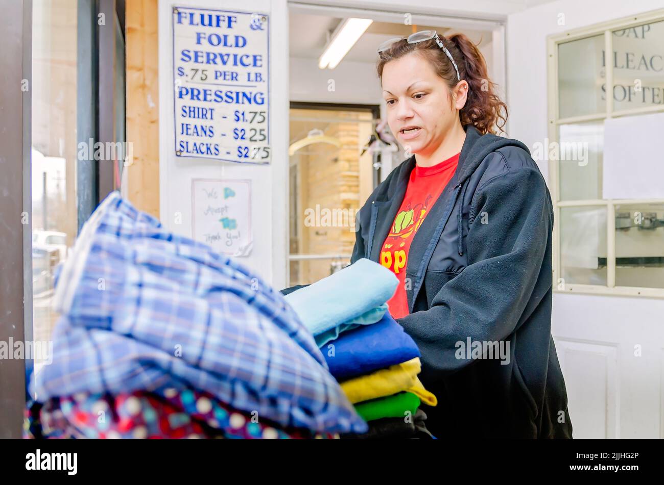 Una mujer dobla la ropa en una lavandería automática, el 23 de febrero de 2013, en Columbus, Mississippi. El trabajo paga el salario mínimo. Foto de stock
