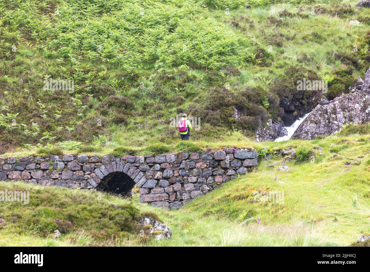 Glencoe Escocia, excursionista pasando por el puente de arco de piedra en el campo alrededor de Glencoe, las tierras altas escocesas en el verano de 2022, Reino Unido Foto de stock