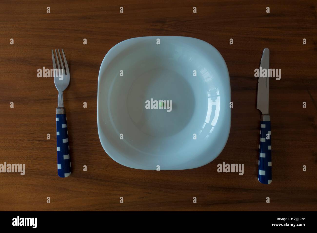 concepto de alta cocina un guisante sobre plato blanco con cuchillo y tenedor sobre mesa de madera Foto de stock
