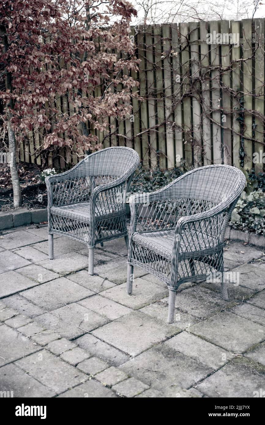 Sillones tejidos fuera en un jardín rústico con plantas otoñales para relajarse después de la jardinería. Patio paisaje con dos sillas de madera en la naturaleza en un Foto de stock