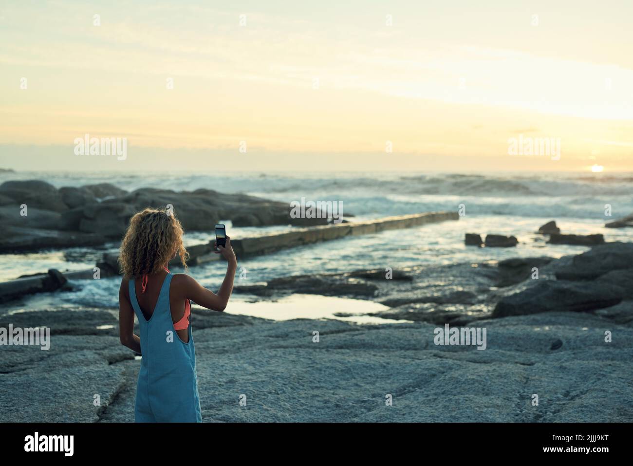 mujer haciendo una foto con el smartphone en una hermosa playa al atardecer compartir estilo de vida de viaje fotografiar mar con cámara de teléfono móvil Foto de stock
