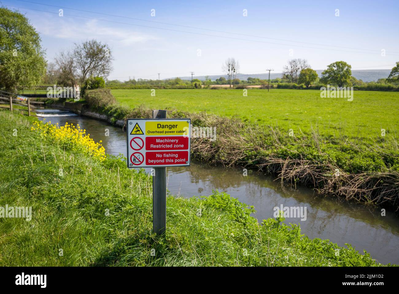Una señal de advertencia de los peligros de los cables eléctricos aéreos en la orilla del río Yeo, también conocido como el Congresbury Yeo, en Iwood cerca del Congresbury, North Somerset, Inglaterra. Foto de stock