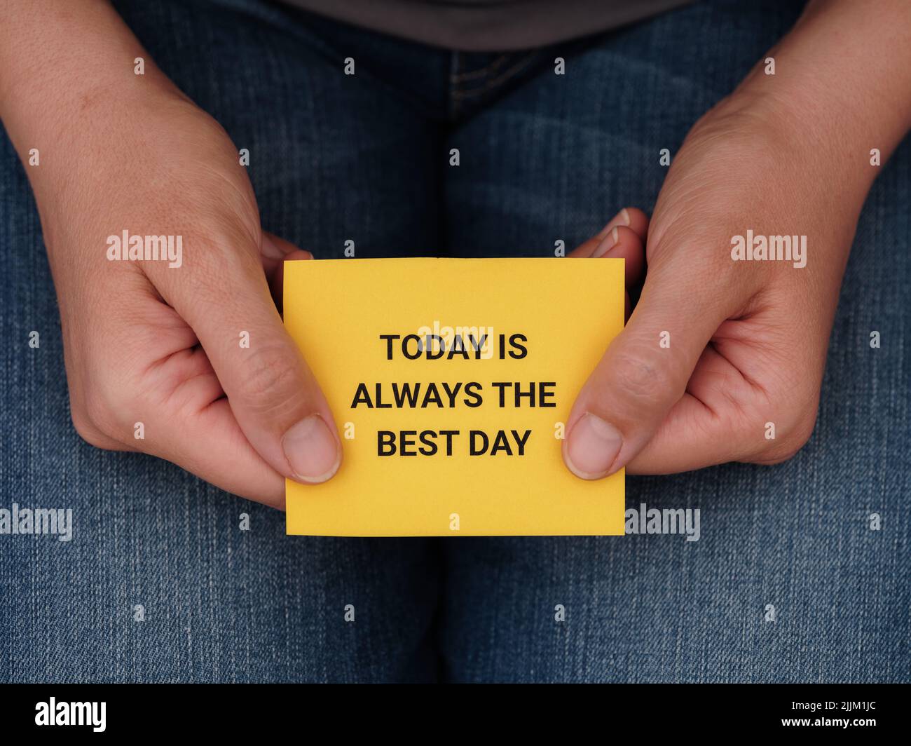 Una mujer sosteniendo un pedazo de papel amarillo con la frase hoy es siempre el mejor día en él en sus manos. Primer plano. Foto de stock