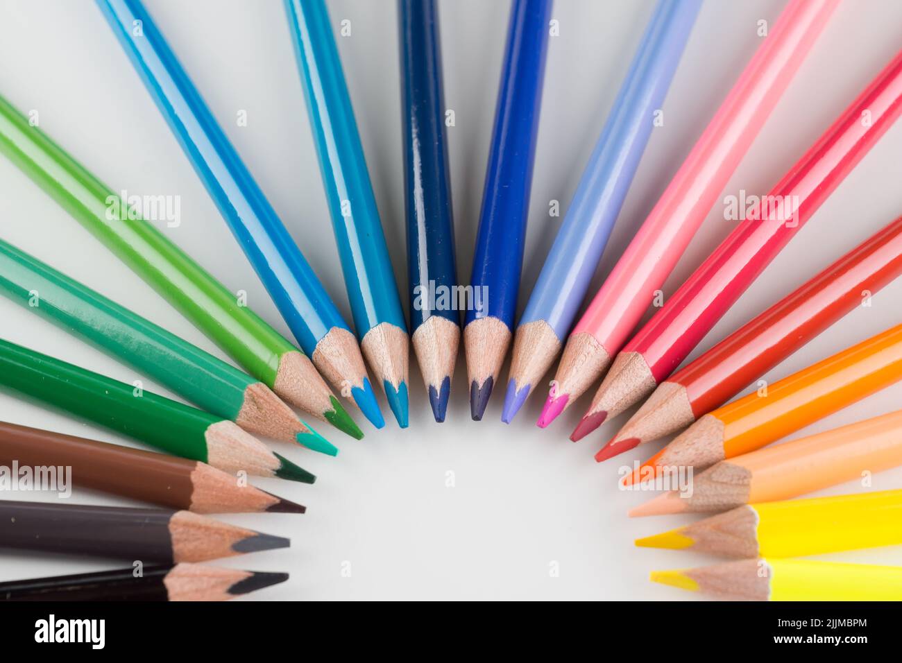 juego de lápices de colores alineados con un arco sobre fondo blanco Foto de stock