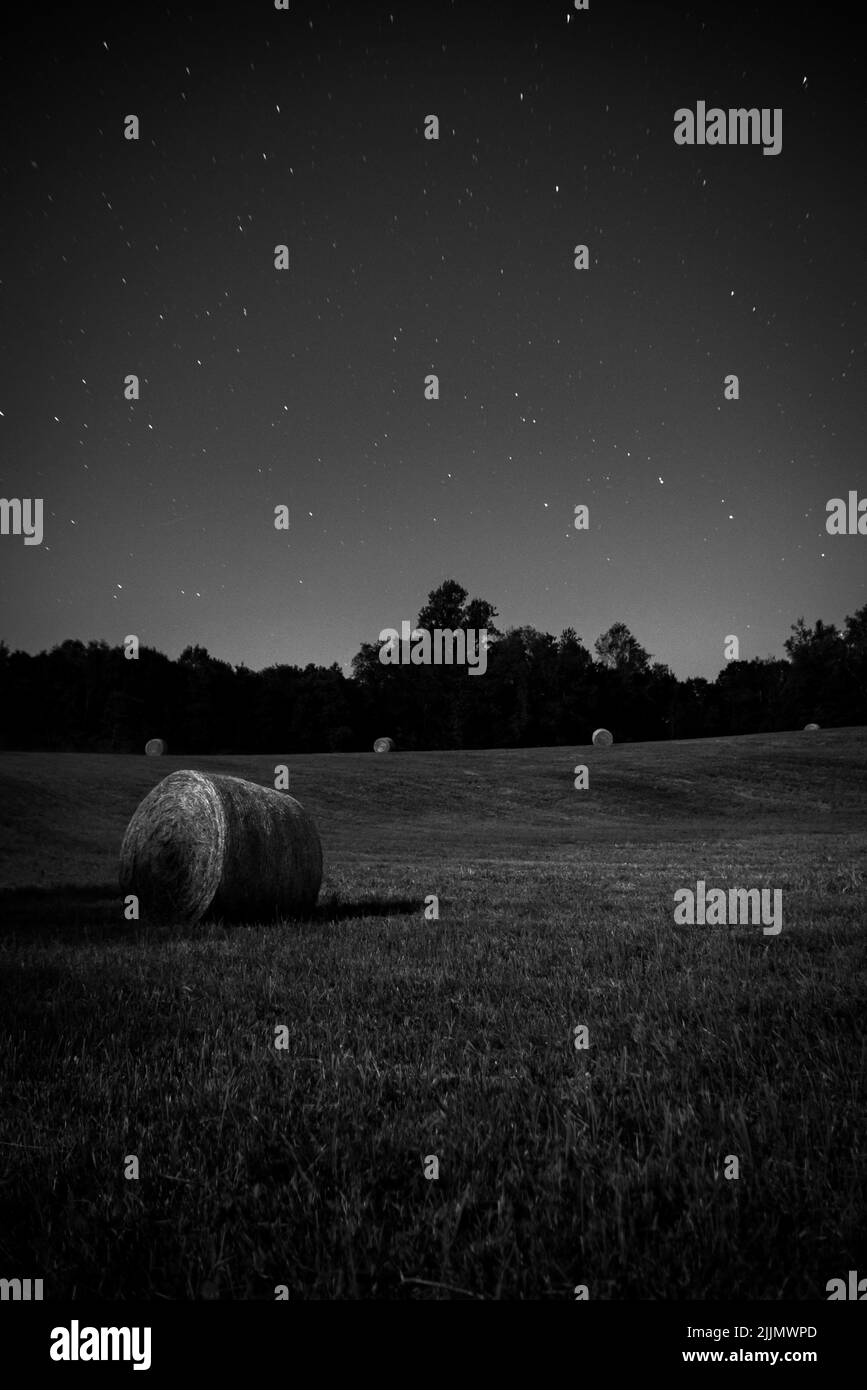 Un tiro vertical de un fardo de heno en un campo con un fondo brillante del cielo por la noche Foto de stock