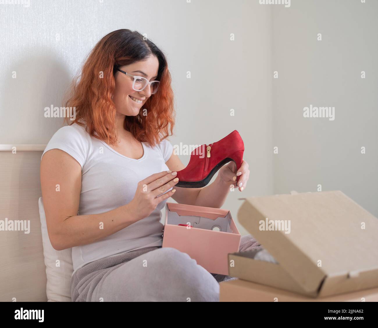 La mujer caucásica abre los zapatos ordenados está sentada en cama. Concepto de compra en línea con entrega a domicilio Fotografía de stock - Alamy